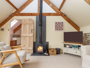 A living room with a wood-burning stove television wooden armchair and exposed wooden beams at The Coach House at Thorn Farm Bridford near Moretonhampstead