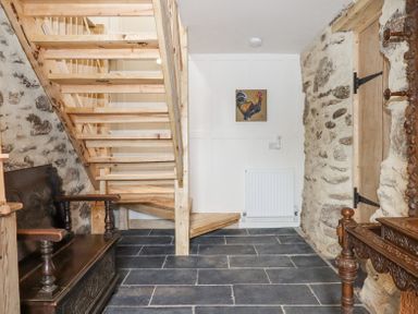 An entryway with a wooden staircase stone walls a dark wooden bench and a carved wooden mirror at The Coach House at Thorn Farm in Bridford near Moretonhampstead