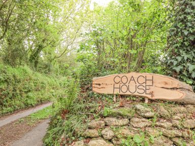 A wooden sign reading Coach House on a stone wall beside a narrow countryside path surrounded by greenery at The Coach House at Thorn Farm Bridford near Moretonhampstead