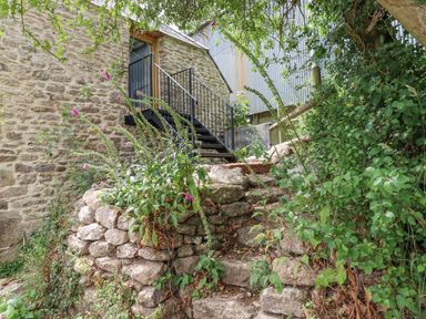 An outdoor stone staircase surrounded by plants leading to a metal staircase and door on a stone building at The Coach House at Thorn Farm Bridford near Moretonhampstead