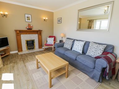 A living room with a blue sofa with cushions a wooden coffee table a red chair a fireplace and a TV at Ceris in Penrhyndeudraeth