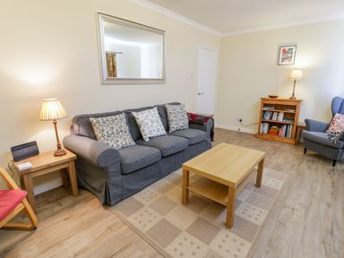 A living room with a gray sofa and cushions a wooden coffee table a wooden side table with a lamp a wooden bookshelf a gray armchair and a framed picture on the wall at Ceris in Penrhyndeudraeth