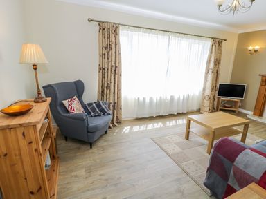A living room with an armchair a wooden coffee table a cabinet with a lamp and a television at Ceris in Penrhyndeudraeth