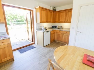 A kitchen with wooden cabinets a round wooden table and an open door leading outside at Ceris Penrhyndeudraeth