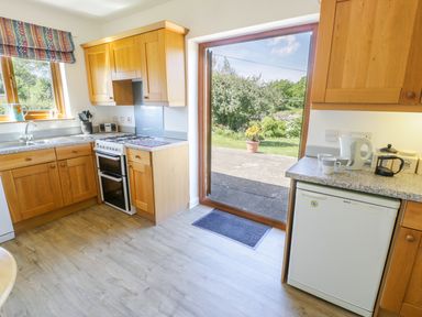 A kitchen with wooden cabinets a gas stove a sink a kettle mugs and a small fridge next to a door leading outside at Ceris in Penrhyndeudraeth