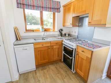A kitchen with wooden cabinets a double sink a gas stove and a dishwasher at Ceris in Penrhyndeudraeth