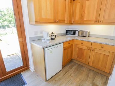 A kitchen corner with wooden cabinets a dishwasher microwave toaster and a kettle near a glass door at Ceris in Penrhyndeudraeth