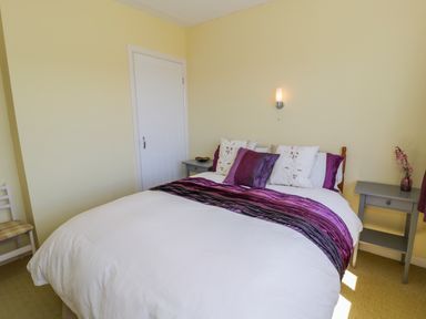 A bedroom with a bed with purple and white bedding two bedside tables a white door and a chair at Ceris Penrhyndeudraeth