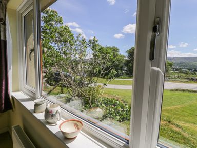 A window sill with ceramic pots and a bowl overlooking a garden with trees and a lawn at Ceris in Penrhyndeudraeth