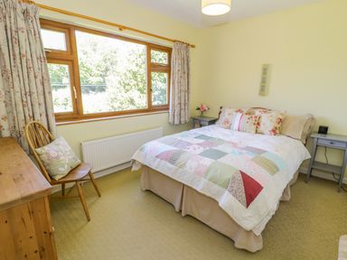 A bedroom with a bed covered with a patchwork quilt beside two small grey tables and a wooden chair at Ceris in Penrhyndeudraeth