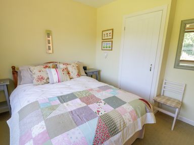 A bedroom with a bed covered in a patchwork quilt and floral pillows two small side tables a white door a chair and a mirror on the wall at Ceris in Penrhyndeudraeth