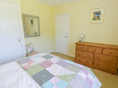 A bedroom with a bed covered by a patchwork quilt a wooden dresser a wall mirror and a small chair at Ceris Penrhyndeudraeth