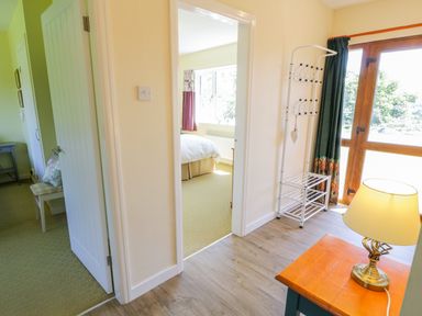 A hallway with a wooden table and lamp next to a coat rack and door leading to a bedroom at Ceris in Penrhyndeudraeth