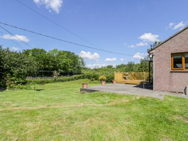 A backyard with a grass lawn and a concrete patio next to a building at Ceris in Penrhyndeudraeth