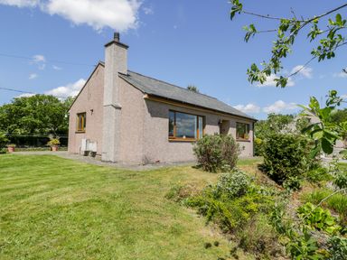 A single-story house with a chimney surrounded by a lawn and plants at Ceris in Penrhyndeudraeth