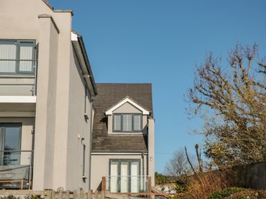 Exterior view of a modern house with balcony and glass railing surrounded by trees and a wooden fence at Seaspray Stoke Fleming Near Dartmouth