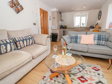 A living room with two sofas a glass coffee table with a bottle and glasses and a kitchen in the background at Seaspray Stoke Fleming Near Dartmouth