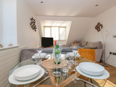 A dining area with a glass table set with plates glasses and cutlery and a living room with a sofa and a television at Seaspray Stoke Fleming Near Dartmouth