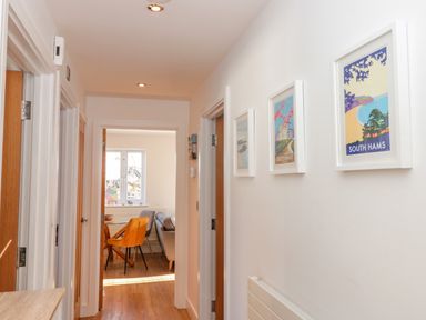 A hallway with three framed pictures on the wall and doors leading to other rooms and a dining area at Seaspray in Stoke Fleming Near Dartmouth