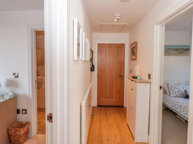 A hallway with wooden flooring a wooden door at the end white walls and a white shoe cabinet on the right