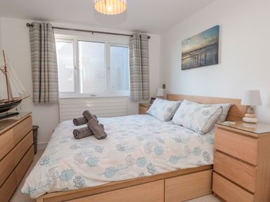 A bedroom with a bed with floral bedding two wooden bedside tables with lamps a chest of drawers a window with curtains and a model boat at Seaspray Stoke Fleming Near Dartmouth
