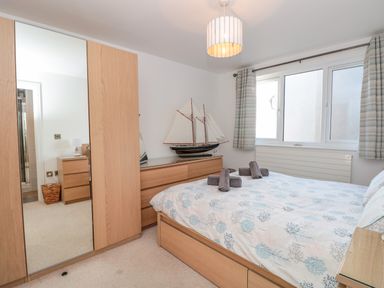 A bedroom with a bed folded towels wardrobe with mirror and model sailboat on dresser at Seaspray Stoke Fleming Near Dartmouth