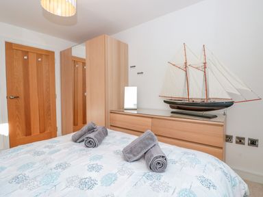 A bedroom with a bed covered with a patterned duvet and rolled towels a wooden wardrobe and chest of drawers with a model sailboat on top at Seaspray Stoke Fleming Near Dartmouth