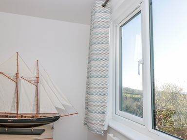 A window with patterned curtains next to a model sailboat in a room at Seaspray in Stoke Fleming Near Dartmouth