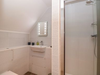 A bathroom with a wall-mounted sink mirror shower and toiletries at Seaspray in Stoke Fleming Near Dartmouth