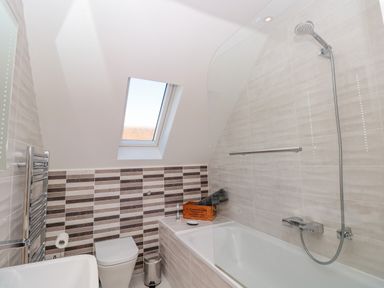A bathroom with a bathtub shower combo a wall-mounted toilet a small window and a towel rack at Seaspray Stoke Fleming Near Dartmouth