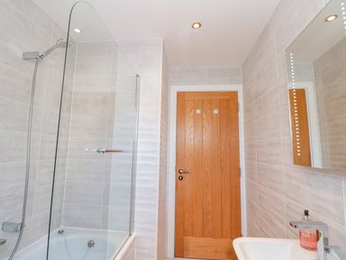 A bathroom with a bathtub shower combination a wooden door and a sink with a soap dispenser at Seaspray Stoke Fleming Near Dartmouth