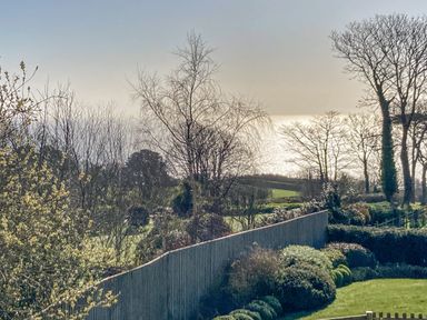 A garden with bushes a wooden fence and leafless trees overlooking fields and a body of water at Seaspray Stoke Fleming Near Dartmouth