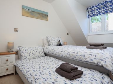 A bedroom with two single beds bedside table and window with patterned blind at Seaspray in Stoke Fleming Near Dartmouth