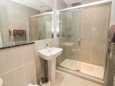A bathroom with a sink a shower with sliding glass doors and a towel on a heated rail at Glenander in Bamburgh