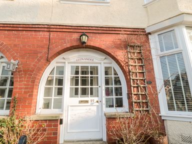 A white front door with glass panels and the number 27 set in a red brick house with an arched entrance at Glenander in Bamburgh