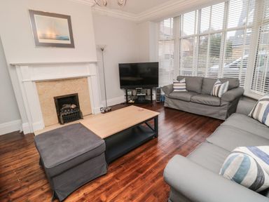 A living room with two gray sofas a wooden coffee table a flat screen tv and a fireplace at Glenander Bamburgh