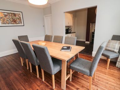 A dining room with wooden table and eight gray chairs at Glenander in Bamburgh