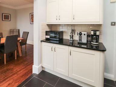 A kitchen with white cabinets black countertop microwave coffee maker and dining area with table and chairs at Glenander in Bamburgh