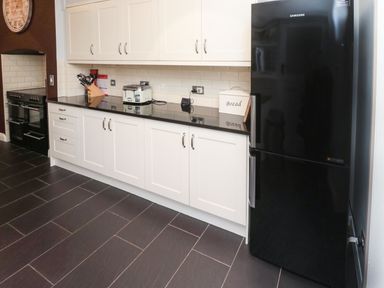 A kitchen with white cabinets black countertop black refrigerator and black stove at Glenander Bamburgh