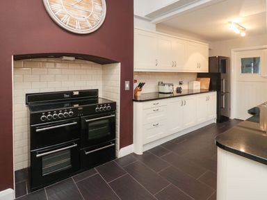 A kitchen with a black stove against a tiled wall white cabinets countertop with toaster knife block and bread box and a black refrigerator at Glenander in Bamburgh