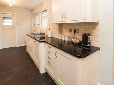 A kitchen with white cabinets black countertop a sink a kettle and storage canisters at Glenander in Bamburgh