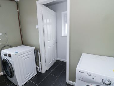 A laundry room with a washing machine dryer and an open door at Glenander Bamburgh