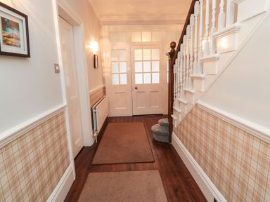 A hallway with patterned wallpaper a staircase with a banister and two rugs on the wooden floor at Glenander in Bamburgh