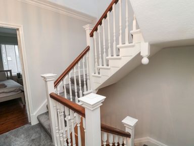 A staircase with white balusters and wooden handrails next to a bedroom at Glenander in Bamburgh