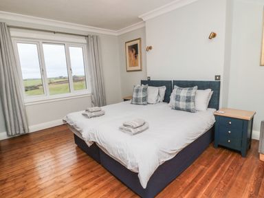 A bedroom with two single beds pushed together with white bedding next to a window and a blue bedside table at Glenander in Bamburgh