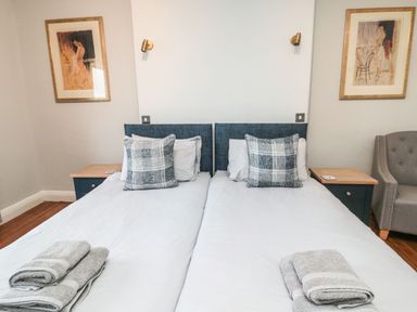 A bedroom with two single beds with pillows and folded towels on them two bedside tables with lamps and framed artwork on the walls at Glenander in Bamburgh