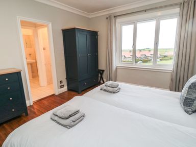 A bedroom with two single beds a wardrobe a chest of drawers and a window showing houses outside at Glenander Bamburgh
