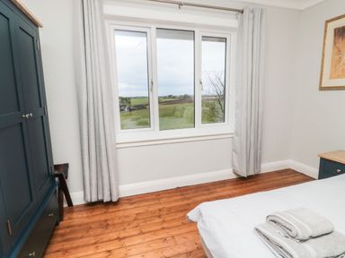 A bedroom with a window showing a countryside view a blue wardrobe and a bed with towels at Glenander in Bamburgh