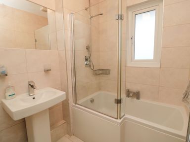 A bathroom with a pedestal sink a bathtub with glass shower screen and a window at Glenander in Bamburgh