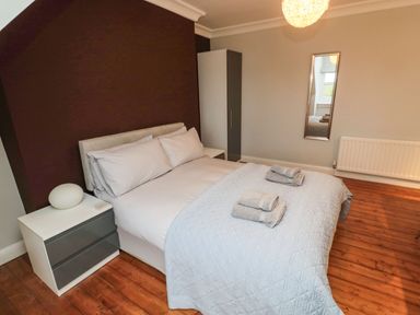 A bedroom with a double bed, two bedside tables, a wardrobe, and a mirror on the wall at Glenander in Bamburgh